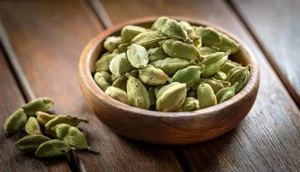 Bol en bois rempli de gousses de cardamome verte sur une table en bois, ingrédient utilisé dans les infusions pour son arôme chaud et ses bienfaits digestifs.