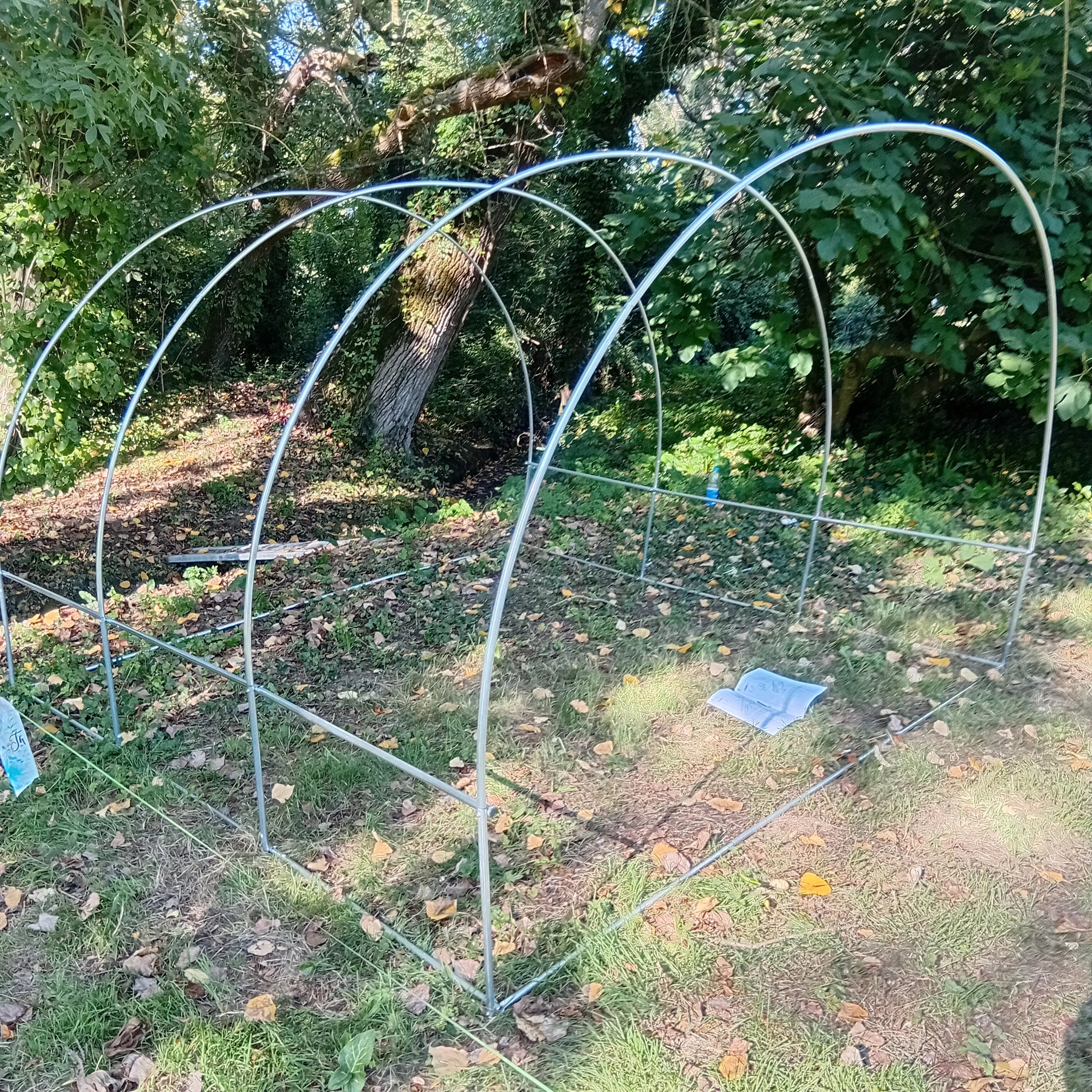 L'armature de base de la mini-serre, composée de tubes métalliques incurvés et droits, en cours d'assemblage sur la pelouse Image