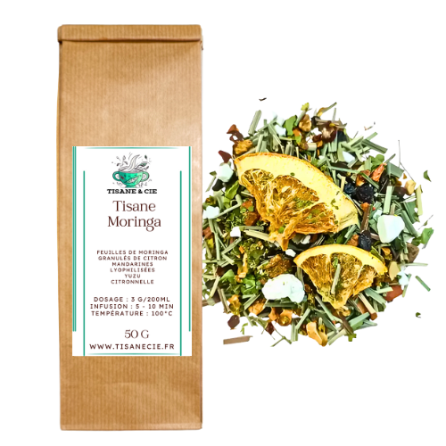 Sachet en papier kraft brun de Tisane Moringa de Tisane & Cie, avec une étiquette verte indiquant les ingrédients (feuilles de moringa, graines de citron, mandarines lyophilisées, yuzu, citronnelle), le dosage et la température d'infusion. À côté du sachet, un tas de la tisane sèche avec des feuilles vertes, des morceaux de fruits lyophilisés jaunes et des herbes aromatiques, formant un mélange de tisane harmonieux.